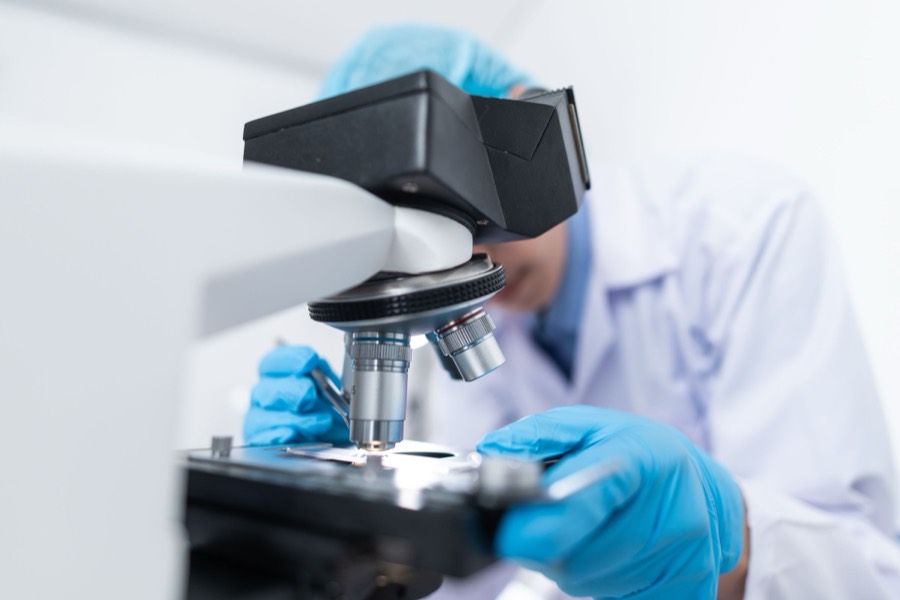 Researcher in white lab coat operating microscope in laboratory